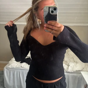 Svart ribbad offshoulder stickad tröja - Säljer en svart stickad tröja med ribbad struktur och offshoulder-design. Tröjan har lång ärm, djup v-ringning och sitter tight men ändå bekvämt. Perfekt för dig som gillar en stilren och trendig look.