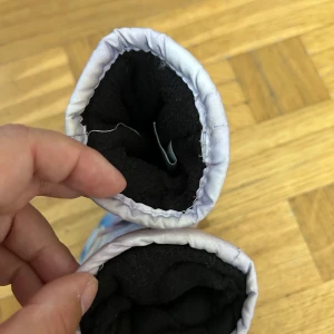 Frozen tumvantar 3-4 år lila blommig - Säljer ett par lila tumvantar från Disney Frozen med blommigt mönster och svarta greppytor i syntetmaterial. Insidan är fodrad med mjuk svart fleece för extra värme. Perfekta för kalla vinterdagar och för små fans av Frost.