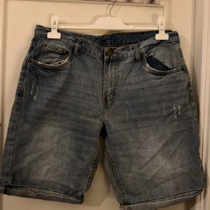 Blå jeansshorts  - Klassiska blå jeansshorts. Shortsens ben är raka och har en casual vibe med uppvikta kanter. Perfekta för varma dagar när du vill ha en avslappnad look.