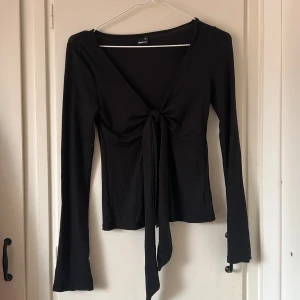 Svart långärmad omlottopp - Svart långärmad topp från Gina Tricot med djup v-ringning och knyt framtill. Toppens omlottdesign ger en snygg och trendig look, perfekt att styla med jeans eller kjol. Mjukt och stretchigt material som sitter skönt på kroppen.