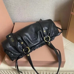 Svart axelväska från Miu Miu i skinn Intressekolll - INTRESSEKOLL Snygg svart axelväska från Miu Miu i mjukt skinn med coola guldfärgade metalldetaljer och ringar. Väskan har en unik form med rynkade detaljer och dubbla axelremmar. Perfekt för dig som vill ha en stilren men ändå edgy accessoar.