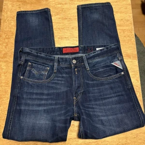 Replay Anbass jeans mörkblå herr - Säljer ett par snygga Replay Anbass jeans i mörkblå tvätt. Klassisk femficksmodell med kontrastsömmar och Replay-logga på fickan. Jeansen har rak passform och är tillverkade i stretchig bomullsdenim för extra komfort.