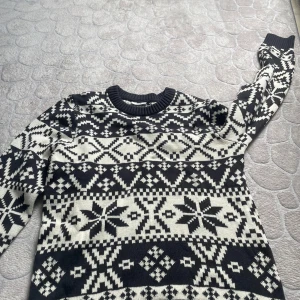 Svartvit stickad tröja från Kappahl - Säljer en svartvit stickad tröja från Kappahl med klassiskt nordiskt mönster. Tröjan har rund halsringning, långa ärmar och ribbade muddar. Perfekt för kalla dagar när du vill ha en snygg och mysig stil. Aldrig använd 