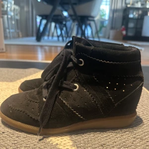 Svarta mockasneakers Isabel Marant - Svarta sneakers från Isabel Marant Étoile i mjuk mocka med snygga broguedetaljer och perforeringar. Skorna har snörning, rund tå och en diskret kilklack för extra höjd. Yttersulan är i gummi och ger en cool kontrast mot det svarta. Kvaliten är bra men har mycket kvar att ge! pris kan även diskuteras.
