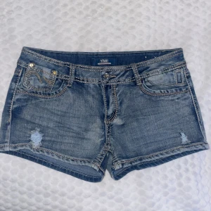 Blå lågmidjade jeansshorts - Snygga blå jeansshorts från YMI med slitna detaljer och kontrastsömmar. Klassisk femficksmodell med låg midja och broderade bakfickor. Perfekta för sommardagar när du vill ha en avslappnad och cool look. 