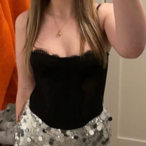 Svart spetskorsett från SHEIN - Snygg svart korsett från SHEIN med spetsdetaljer och tunna axelband. Toppen har markerade sömmar, bygel och hakknäppning bak. Materialet är syntet och spets, och modellen är tight och figurnära.