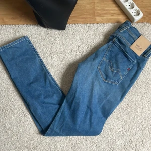 Replay Hyperflex blå jeans - Säljer ett par blå Replay Hyperflex jeans med klassisk femficksdesign och snyggt skurna ben. Jeansen är i stretchigt material som ger en bekväm passform och har en modern, smal siluett. Perfekta för dig som gillar stilrena och flexibla jeans.