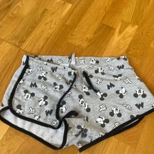 Disney shorts  - Grå shorts med svart-vita Mickey Mouse-motiv från Disney och FB Sister. De har svarta kanter och snörning i midjan. Perfekta för chill dagar eller som pyjamasshorts. Mjukt bomullsmaterial och relaxed fit.