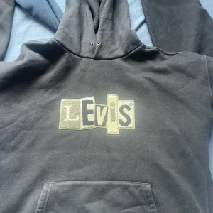 Svart hoodie från Levi's med broderad logga - Svart hoodie från Levi's med stor logga i grå och beige toner på bröstet. 