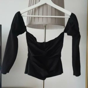 Svart offshoulder topp från Boohoo - Säljer en svart offshoulder topp från Boohoo med långa ärmar och snygg drapering baktill. Toppen har en figurnära passform och är perfekt för dig som vill ha en trendig och stilren look. Materialet är mjukt och stretchigt för extra komfort.
