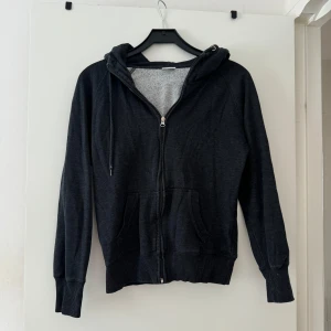 Svart hoodie med dragkedja och huva - Mysig svart hoodie från Cubus i storlek M. Tröjan har dragkedja framtill, två fickor och en skön huva med snörning. Insidan är mjukt fodrad och materialet känns som bomullsmix. Perfekt för chill dagar eller när du vill vara extra bekväm.