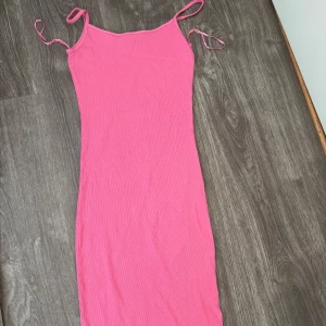 Rosa tight långklänning med smala band - En enkel och snygg rosa kortklänning med smala axelband. Klänningen har en tight passform och är perfekt för varma dagar. Materialet känns mjukt och stretchigt, vilket gör den bekväm att bära hela dagen.