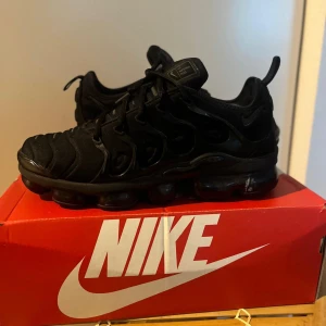 Nike Air Vapormax Plus helsvarta sneakers - Nike Air Vapormax Plus i helsvart med futuristisk design och synlig bubbelsula. Ovandel i syntet och textil med coola detaljer och snörning. Perfekta för dig som vill sticka ut med en modern och sportig look.