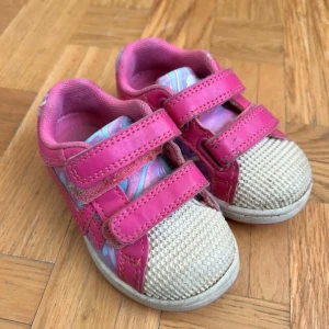 Färgglada sneakers med kardborre, strl 21 - Söta sneakers i rosa med färgglada mönsterdetaljer i blått och lila. Skorna har två praktiska kardborreband och tåparti i beige mesh. Perfekta för lek och spring, med mjuk insida och platt sula.