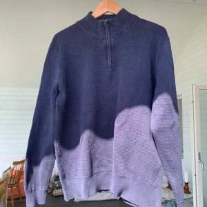 Mörkblå stickad tröja med half zip - Mörkblå stickad tröja med hög krage och half zip-dragkedja framtill. Tröjan har en grovstickad struktur och långa ärmar, perfekt för kyligare dagar. Enkel och stilren design som funkar till det mesta.