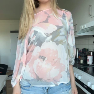 Blommig blus i pastellfärger - Säljer en luftig blus med stora blommor i rosa, grått och beige. Blusen har transparent tyg, lös passform och långa ärmar. 