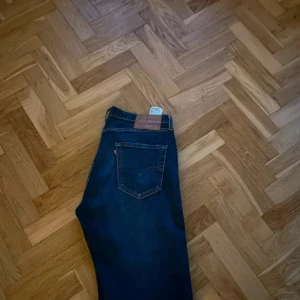 Levi's 501 mörkblå jeans 32/32 - Klassiska Levi's 501 jeans i mörkblå denim med raka ben och femficksmodell. Snyggt läderpatch bak i midjan och ikonisk röd Levi's-tagg på bakfickan. Perfekta för en clean och tidlös look.