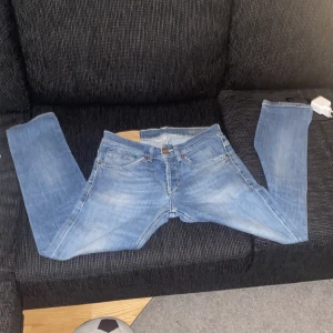 Dondup jeans slim fit  - Säljer ett par ljusblå jeans med klassisk femficksdesign och raka ben. Jeansen har snyggao slitningar och kontrastsömmar på bakfickorna. Perfekta för dig som gillar en avslappnad och tidlös look.
