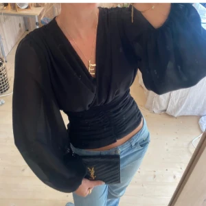 Svart omlottblus  - Supersnygg svart omlottblus med v-ringning och ballongärmar. Blusen har rynkade detaljer framtill.  Har en vit likadan längre ner i flödet💞