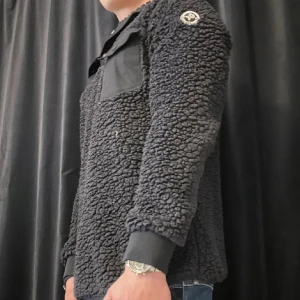 Svart teddyjacka från Pelle p - Säljer en svart teddyjacka från Pelle p med mjuk, fluffig yta och en bröstficka i kontrasterande tyg. Jackan har lång ärm, ribbade muddar och klassisk patch på axeln. Perfekt för dig som gillar streetwear och vill hålla dig varm.