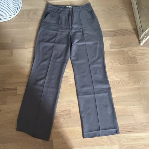 Grå kostymbyxor från Madlady - Snygga grå kostymbyxor från Madlady med raka ben och pressveck. Byxorna har normal midja, hällor för bälte och sidfickor. Perfekta för en clean och stilren look. Materialet känns mjukt och följsamt.