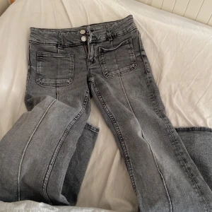 Grå jeans från Gina Tricot, storlek 152 - Snygga grå jeans från Gina Tricot med utsvängda ben och stora framfickor. Jeansen har dubbla knappar i midjan och klassiska bakfickor. Perfekta för dig som gillar en avslappnad och trendig look.