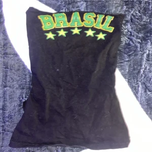Svart Brasil tubtopp med stjärnor - Cool svart tubtopp med texten 'BRASIL' i grönt och gult samt fem gröna stjärnor framtill. Baksidan har snygga rynkade detaljer som ger extra edge. Perfekt för dig som vill sticka ut