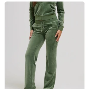 Gröna velourbyxor Juicy Couture - Mysiga gröna mjukisbyxor från Juicy Couture i velour med bred resår och snörning i midjan. Byxorna har raka ben, stora fickor fram och bak med knappdetaljer samt broderad logga på ena fickan. Perfekta för chill eller streetstyle. Aldrig använda 