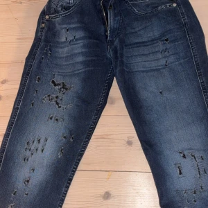 Mörkblå slitna jeans från Replay - Säljer ett par mörkblå jeans från Replay med snygga slitningar och distressed detaljer på benen. Klassisk femficksmodell med dragkedja och knapp. Jeansen har en modern look och passar perfekt till sneakers eller boots.