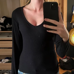 Svart ribbad tröja från 157 - Svart långärmad tröja från 157 med snygg v-ringning. Tröjan är ribbad och har en tight passform som sitter riktigt snyggt. Perfekt att matcha med jeans eller kjol för en clean look.