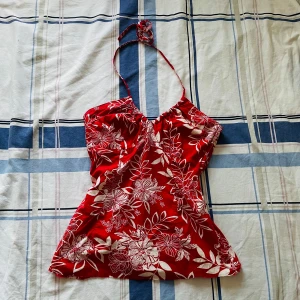 Röd topp - Röd linnetopp med vita blommor och blad på sig. V ringad och är knuten vid nacken. Är från H&M och i storlek 38. Har en dragkedja vid sidan, aldrig använd och är perfekt för sommaren🤭