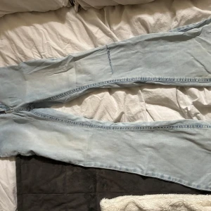 Ljusblå raka jeans med råa kanter - Säljer ett par ljusblå jeans med ytsvängd passform och råa, fransiga benslut. Jeansen har klassiska bakfickor och är tillverkade i mjukt denimtyg. Perfekta för en avslappnad och trendig look. Lågmidjade. Defekter längst ner