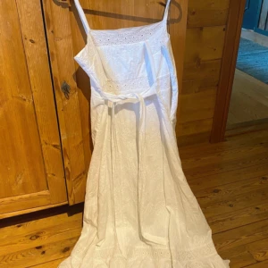 Vit långklänning från Bikbok - Superfin vit långklänning från bikbok med broderade detaljer och smala axelband. Klänningen har ett knytband i midjan och vackra spetsinslag upptill och nertill. Perfekt för sommarens alla tillfällen! Står storlek L men är helt klart en xs