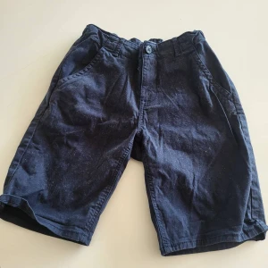 Mörkblå shorts från Lindex - Snygga mörkblå shorts från Lindex med klassisk passform. De har sidfickor, bakfickor och stängs med knapp och dragkedja. Perfekta för varma dagar och enkla att matcha med det mesta. Gjorda i mjuk bomull för skön känsla hela dagen.