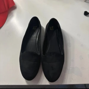 Svarta mocka ballerinaskor från XIT - Stilrena svarta ballerinaskor från XIT i mjuk mocka-look. Skorna har rund tå och platt sula, perfekt för dig som gillar en enkel och klassisk stil. Passar till det mesta och är lätta att matcha med olika outfits.