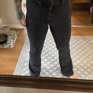 Svarta high waist jeans med knappar - Snygga svarta jeans med hög midja och raka ben. Jeansen har stora framfickor och flera knappar framtill istället för dragkedja. Materialet är klassisk denim och passformen är normal med en rak siluett.