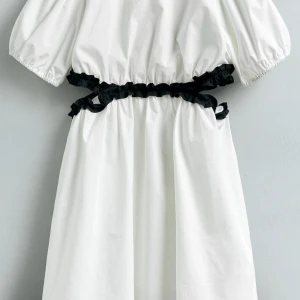 Vit kortklänning med svarta detaljer - Supersöt vit kortklänning med puffärmar och svarta volangdetaljer runt midjan. Klänningen har en luftig passform och knäpps med en knapp i nacken🥰🥰🥰storlek 164 men passar s & prislapp kvar 