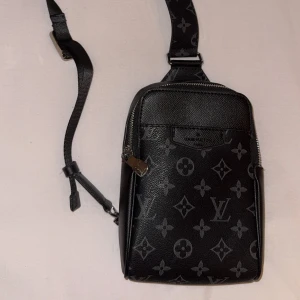 Luis vyutton svart axelväska i skinn - Säljer en svart axelväska  med klassiskt monogrammönster. Väskan har justerbar rem, silverfärgade dragkedjor och är tillverkad i skinn. Perfekt storlek för mobilen och andra småsaker, och ger en lyxig vibe till din outfit.