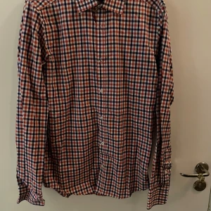 Rutig skjorta från Boomerang  - Snygg rutig skjorta från Boomerang i storlek XS. Skjortan har ett klassiskt rutmönster i rött, blått och vitt, långa ärmar och knäppning framtill. Perfekt för dig som gillar en preppy stil och vill sticka ut med färg.