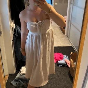 Strandklänning - Superfin beige axelbandslös klänning med knyt framtill. Perfekt till stranden eller när man vill ha nått lätt. 