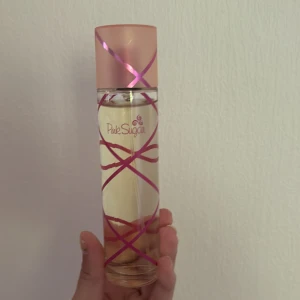 Pink Sugar Eau de Toilette 100ml - Söt och lekfull parfym från Pink Sugar i en genomskinlig glasflaska med rosa detaljer och lock. Flaskan rymmer 100 ml och har ett unikt mönster med rosa band runt om. Perfekt för dig som gillar söta och ungdomliga dofter. Enbart använd ett fåtal gånger.