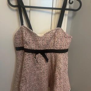 Top med rosett och struktur - Supersöt Top i strukturerat tyg med rosa, svarta och vita toner. Axelbandsmodell med svarta band och en svart rosett i midjan. Toppen har dragkedja bak. Aldrig använd men har tyvärr tagit bort prislappen. Köpt på Zara men helt slutsåld om jag kommer ihåg rätt. 