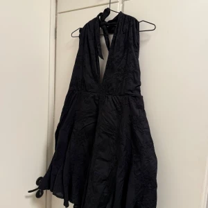 Svart kortklänning  - Svart kortklänning med brodyr ifrån bikbok, superfin klänning men dom inte längre används. Knyte i nacken och även i midjan och öppen rygg, storlek L