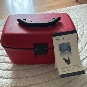 Röd resväska Carlton med kodlås - Säljer en röd resväska från Carlton med hårt skal, kodlås och praktiskt bärhandtag. Insidan har elastiska fack och en löstagbar plastbricka för småprylar. Perfekt för dig som vill resa smidigt och hålla ordning på dina grejer.