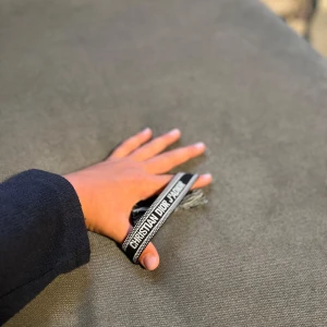 Christian Dior svart/vitt armband - Snyggt armband från Christian Dior i svart och vitt med tydlig logga och coola fransdetaljer. Armbandet är vävt i tyg och har texten 'CHRISTIAN DIOR J'ADIOR' broderat. Perfekt accessoar för att lyfta din outfit.