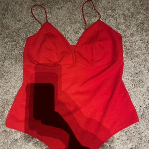 Röd linnebody med smala axelband - Snygg röd linnebody med smala axelband och v-ringad front. Perfekt för dig som vill ha en enkel men ändå iögonfallande topp. Sitter tight och har en klassisk, stilren look som passar till jeans eller kjol.