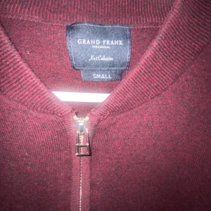 Vinröd kofta från Grand Frank - Snygg vinröd kofta från Grand Frank med hel dragkedja framtill. Tröjan är stickad och har en klassisk rund halsringning samt långa ärmar. Perfekt för lager-på-lager och enkel att matcha med olika outfits.