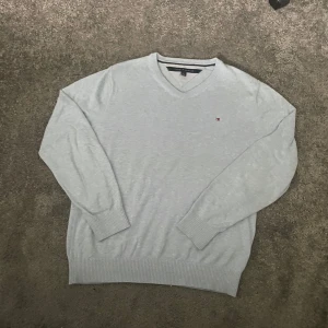 Ljusblå v-ringad tröja Tommy Hilfiger - Snygg ljusblå v-ringad tröja från Tommy Hilfiger med liten broderad logga på bröstet. Tröjan är i mjuk bomull, har ribbade muddar och klassisk passform. Hör av er vid frågor eller funderingar