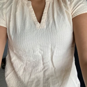 Beige blus från Saint Tropez - Säljer en ljusbeige blus från Saint Tropez i storlek M. Blusen har korta ärmar, v-ringning och ett subtilt vågigt mönster i tyget. Perfekt för dig som gillar en enkel men ändå snygg stil. Har aldrig använt❤️