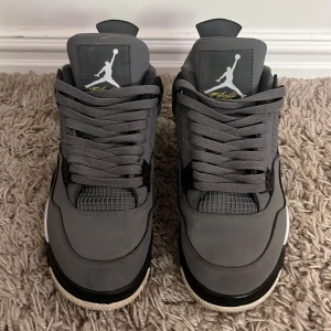 Nike Air Jordan 4 Cool Grey sneakers - Nike Air Jordan 4 Cool Grey med grå ovandel i skinn och mesh, svarta och vita detaljer samt gula accenter på sulan och tungan. Perfekt för dig som gillar streetwear. Pris kan diskuteras. 